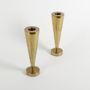 Two brass cone-shaped candle holders on a white background