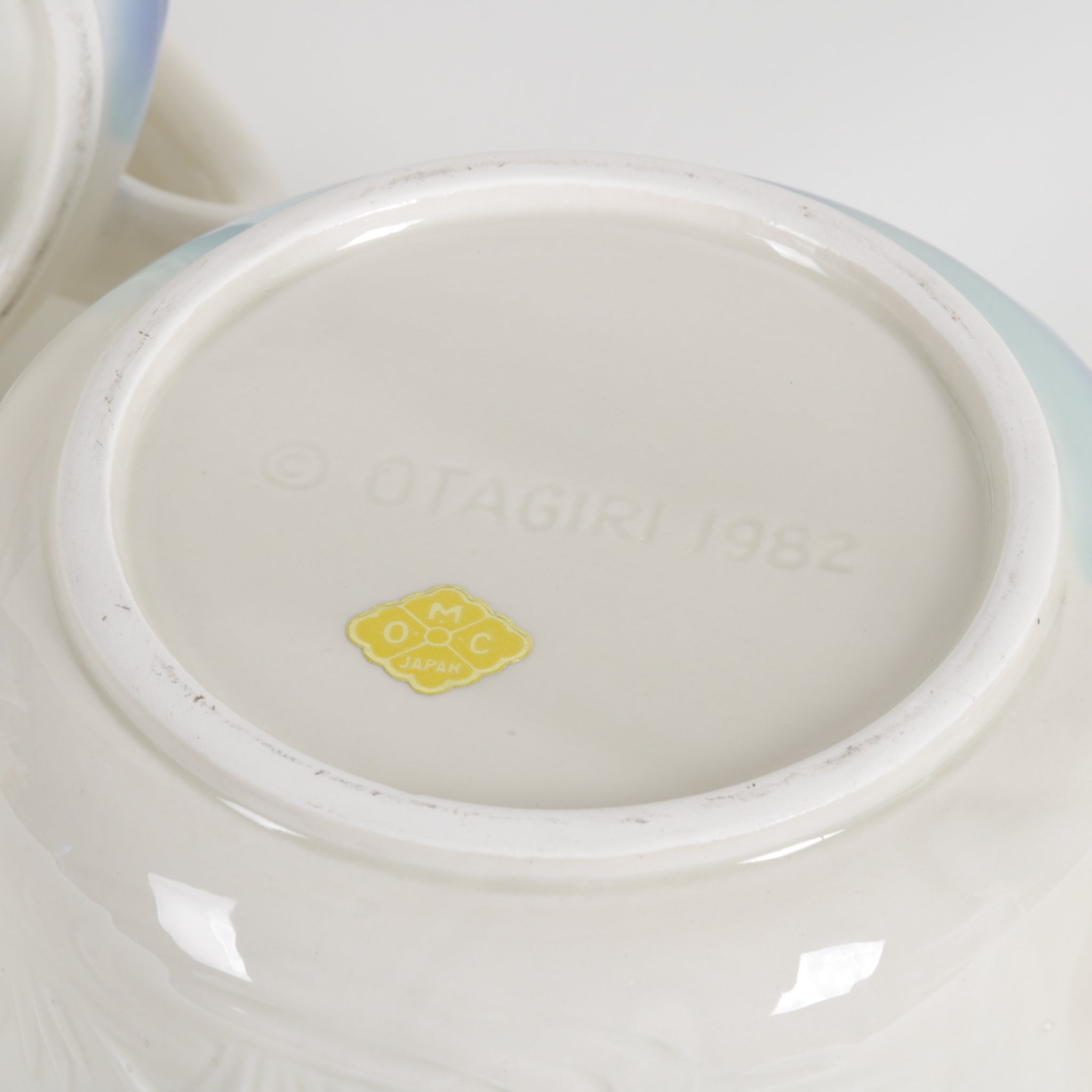 Close-up of a ceramic mug bottom with a visible brand logo OMC Japan and text on a white background