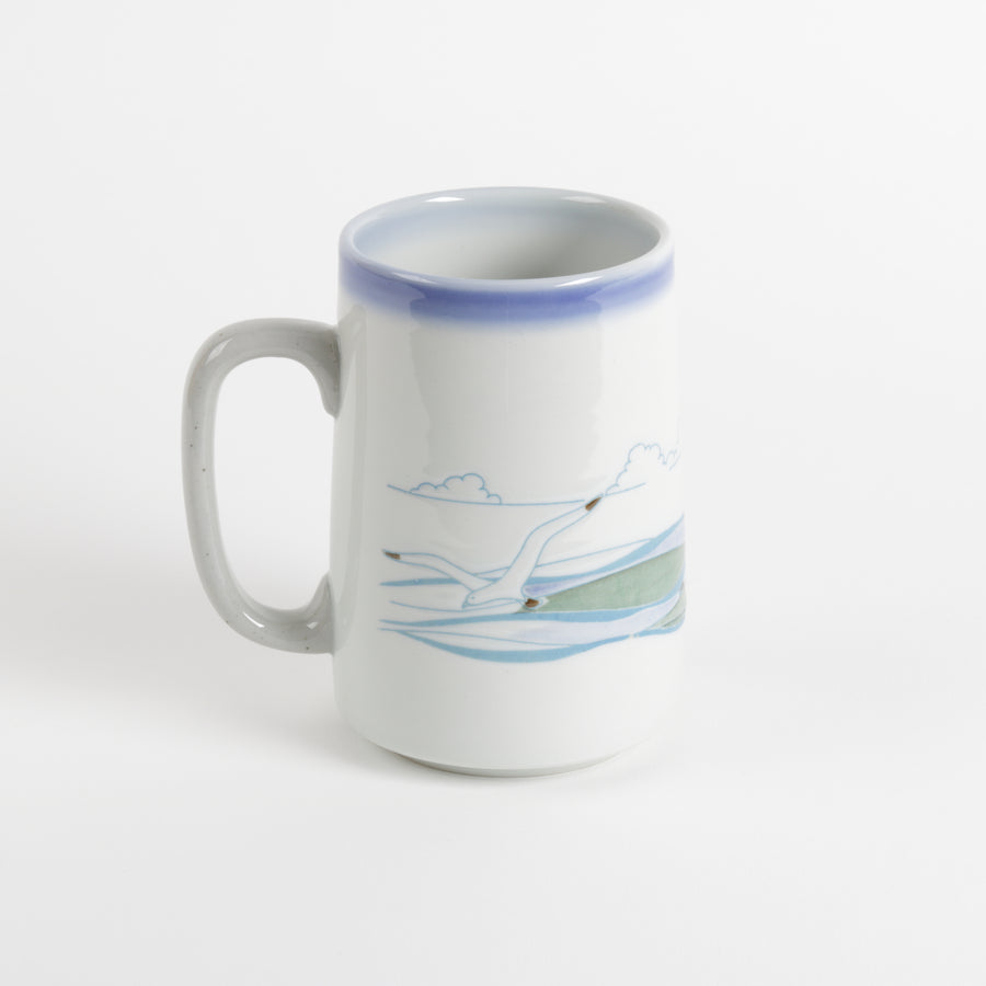 Tall ceramic coffee mug with seagulls in the foreground and horizon