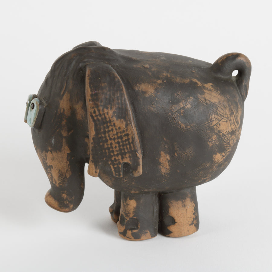 Ceramic elephant sculpture with brown body and blue eyes against white background