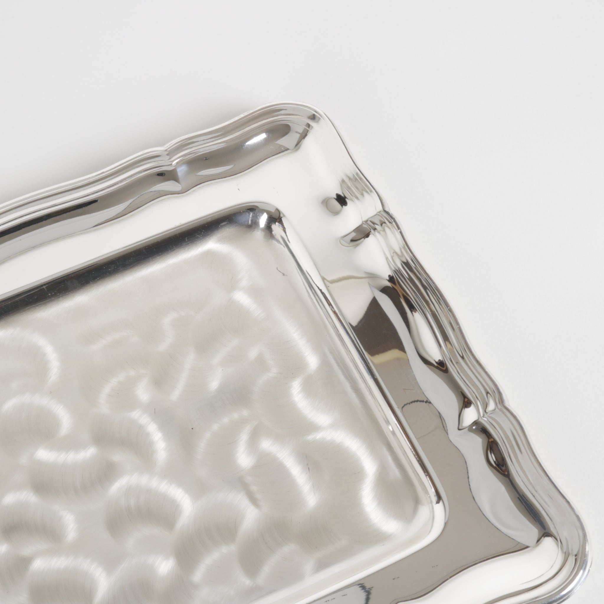 Silver tray with textured surface and wavy edges on a light gray background