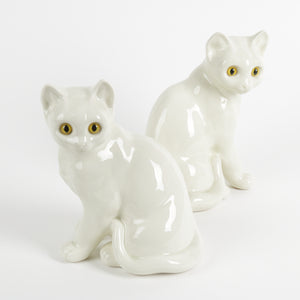 Two white ceramic cat figurines with amber yellow eyes