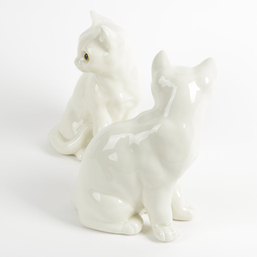 Two white ceramic cat figurines with amber yellow eyes